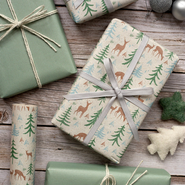 Gifts wrapped in festive paper with deer and tree patterns on a wooden surface.