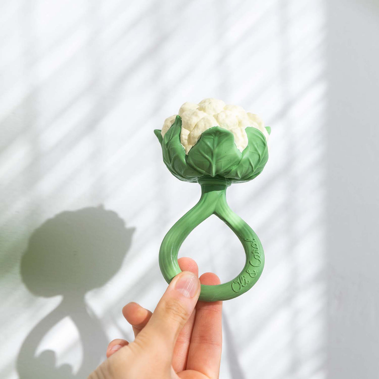 Green natural rubber teething ring in the shape of a cauliflower held by a hand against a white background