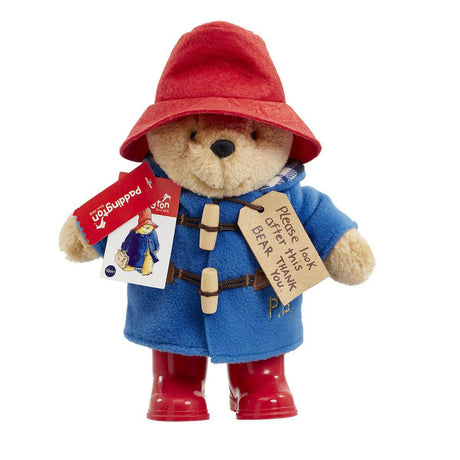 Stuffed toy Paddington Bear with red hat, blue coat, and red boots on a white background.