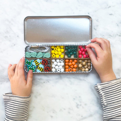 Children's hands opening a small metal box filled with colorful beads and small toys on a marble surface.