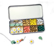 Colourful beads and floral elements in a divided tin on a white background