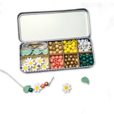 Colourful beads and floral elements in a divided tin on a white background
