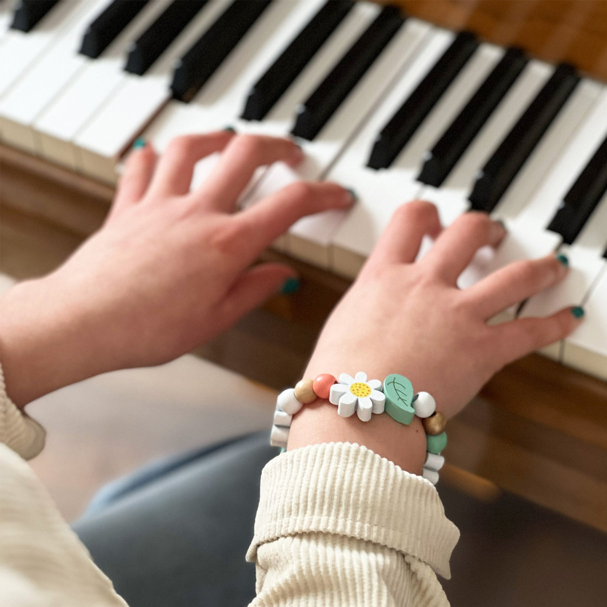 Close-up of hands playing a piano with a bracelet featuring daisy flowers and leaves