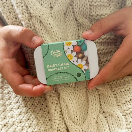 Cotton Twist Daisy Chain Bracelet Kit held by hands on a knitted fabric background