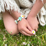 Child's hands wearing a bracelet with flowers on a grassy background