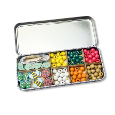 Cotton Twist open tin box with compartments containing colourful beads and decorative items on a white background