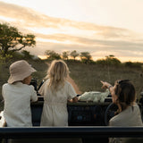 Two children and a woman in a safari vehicle observing wildlife in a grassy field with a soft crocodile toy sitting on the dashboard