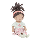 Soft doll with floral pink and sage green dress, pink headband and sage green socks with pink pompoms. Curly brown hair tied in a ponytail.