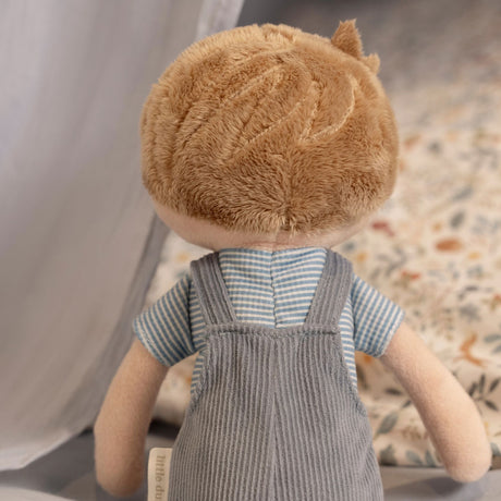 back view of a male soft doll with blonde hair, blue overalls and a stripey blue t-shirt.