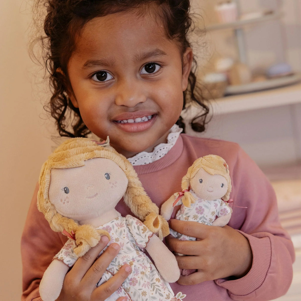 Child holding two soft dolls one large and the other small