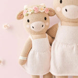 Knitted soft toy cows with a pale pink dresses and floral pink and cream headband on a pink background