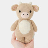 Knitted Baby Jersey cow toy held in a hand against a white background