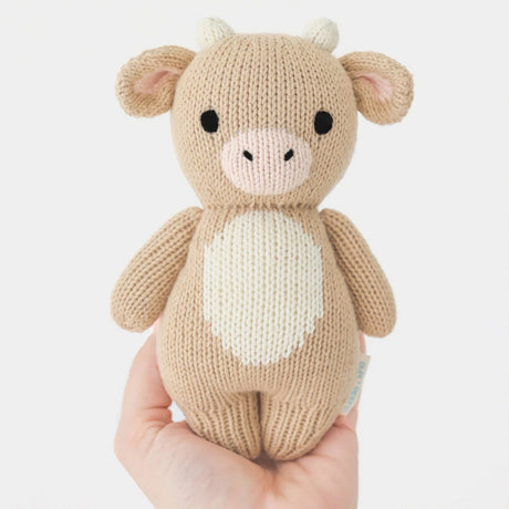 Knitted Baby Jersey cow toy held in a hand against a white background