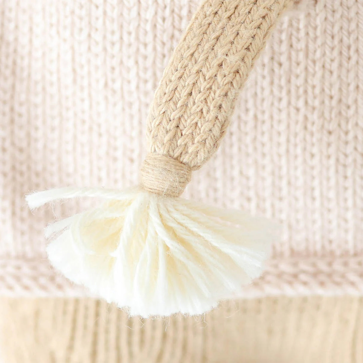 Close-up of a woven handle with a tassel on a textured beige background