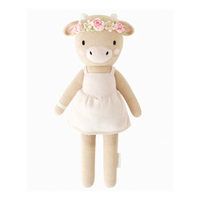 Knitted soft toy cow with a pale pink dress and floral pink and cream headband on a white background