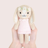 Hand Knitted bunny toy with a pink dress in front of a floral-patterned box on a white background