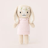 Knitted bunny toy with a pink dress on a light beige background