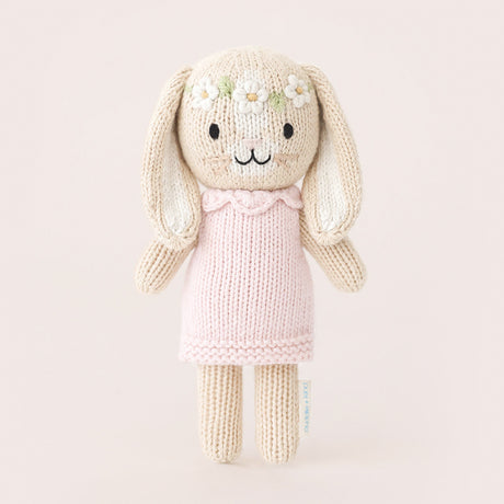 Knitted bunny toy with a pink dress on a light beige background