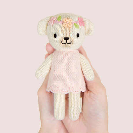 Knitted dog with a pink dress held in a hand against a light pink background