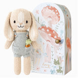 nitted bunny toy in a blue dunagree outfit with carrots in his pocket with a decorative box featuring floral and mushroom designs.