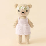 Knitted teddy bear wearing a pink dress with a flower headband on a beige background