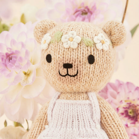 Knitted teddy bear with flower decorations in front of flowers