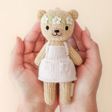 Hand holding a small knitted bear toy with a dress against a beige background
