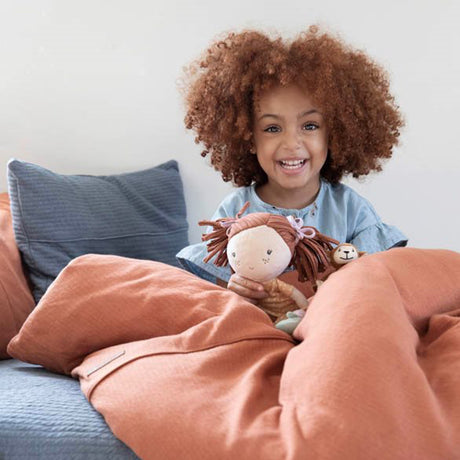 Child holding a soft rag doll on a bed with brown bedding and blue pillows.