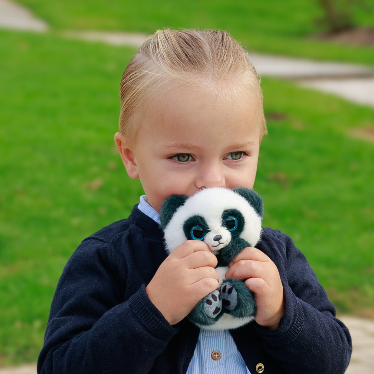 A young child holding a plush panda toy against their face with a blurred green grassy background.