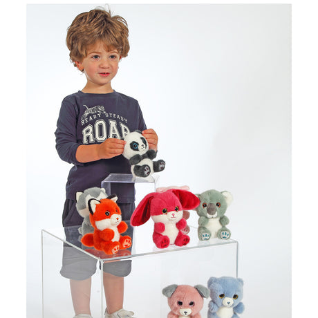 A young boy stands behind a clear acrylic display table holding a plush panda, with several colourful stuffed animals arranged on the table