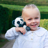 A young girl holding a small black-and-white panda plush toy outdoors