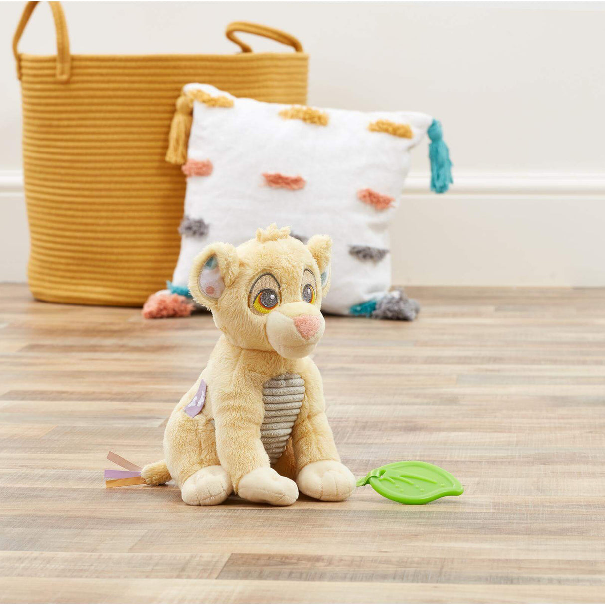Plush baby toy of a lion cub Simba from Disney's 'The Lion King' with green teether leaf attached on a wooden floor