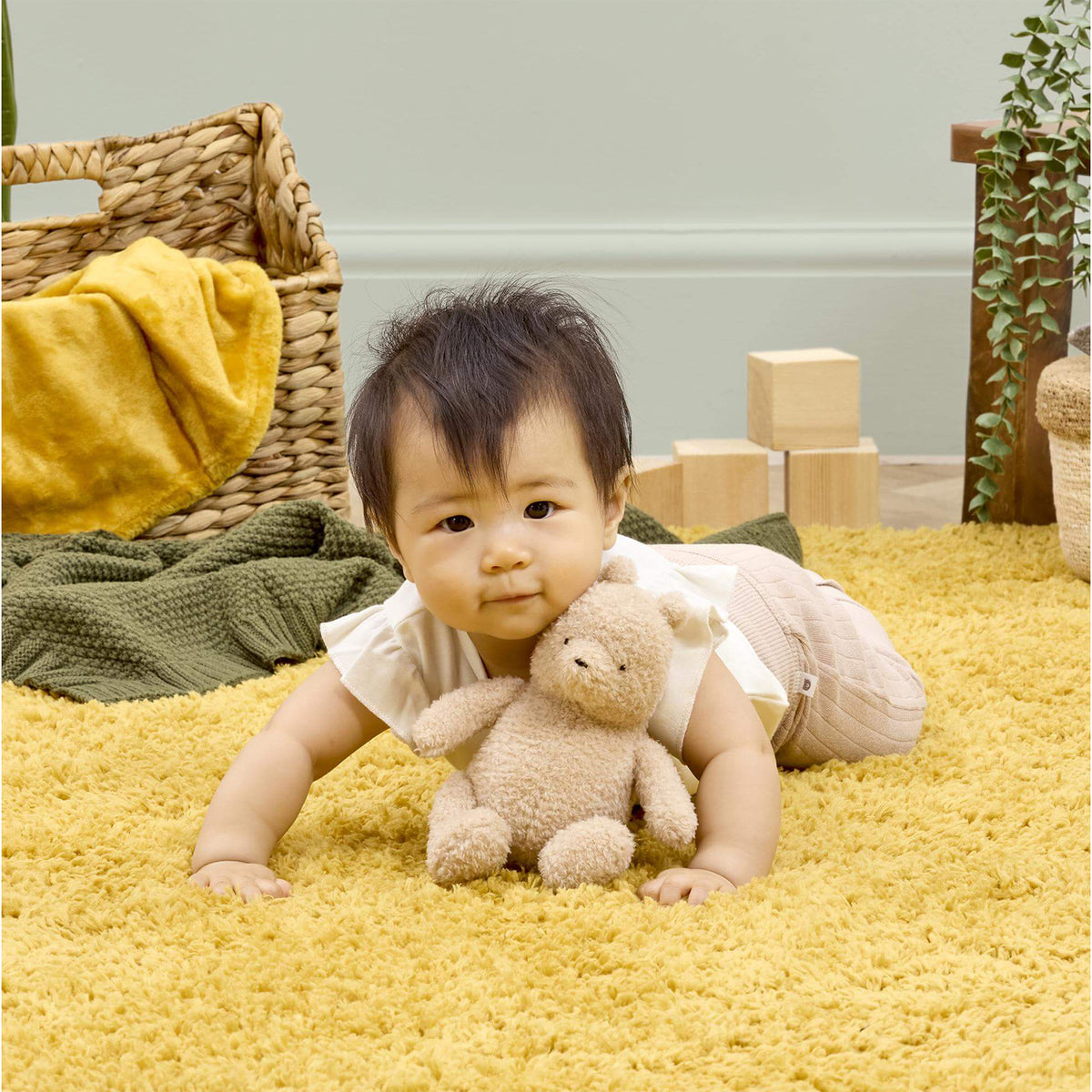 Baby lying on yellow rug cuddling Winnie the Pooh 100 soft small toy