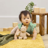 Baby sitting on yellow rug holding Winnie the Pooh 100 soft small toy in nursery setting