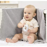 Baby sitting on a bed holding a Plush Dobby ring rattle toy, with a neutral background