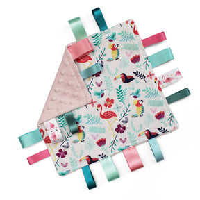 A square baby comforter featuring a colourful tropical print of flamingos, toucans, and foliage on a white with a pink minky dot reverse side and colourful matching satin ribbon tabs.