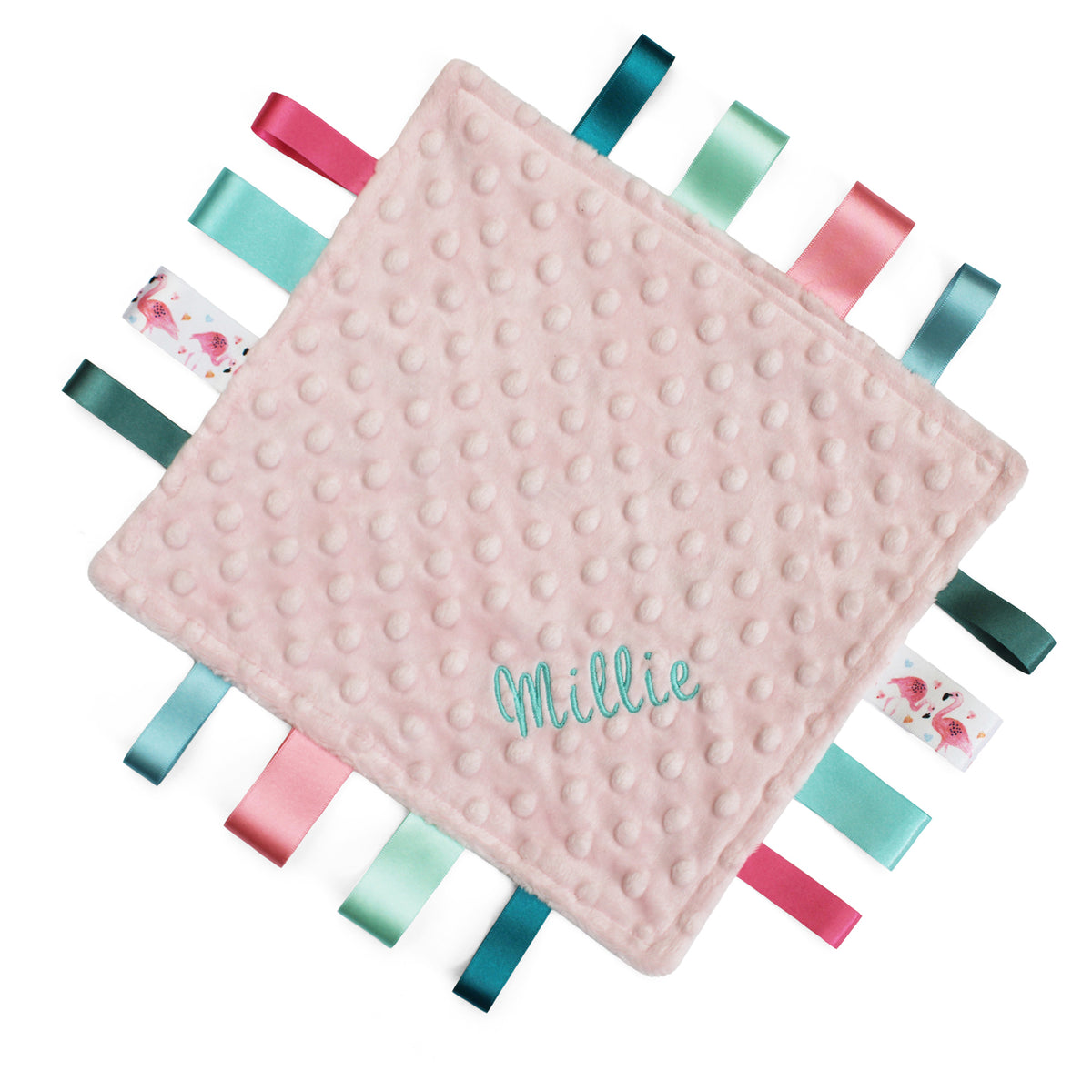 A square pink minky baby comforter with a textured bubble surface, personalized with the name in teal script. The edges feature colourful satin ribbon tags in shades of teal, pink, and green, with two tags showing small pink flamingos