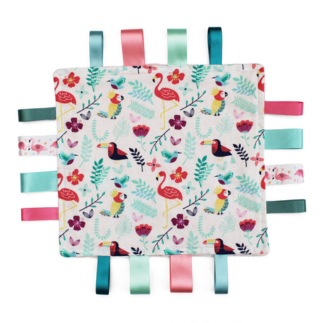 A square fabric sensory baby soother with a colourful tropical pattern featuring flamingos, toucans and leaves on a white background, finished with eight hanging ribbon tabs in teal, pink, mint, and dark green.