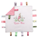 A personalised ribbon taggy blanket with a Flopsy bunny design, featuring a white or cream background with pink / green ribbon tags. The blanket has a Dimple Minky back in pink, white, cream  green or and includes decorative satin  tags with a variety of patterns.