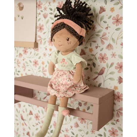 Soft doll with floral pink and sage green dress, pink headband and curly brown hair tied in a ponytail against a floral bird wallpapered background