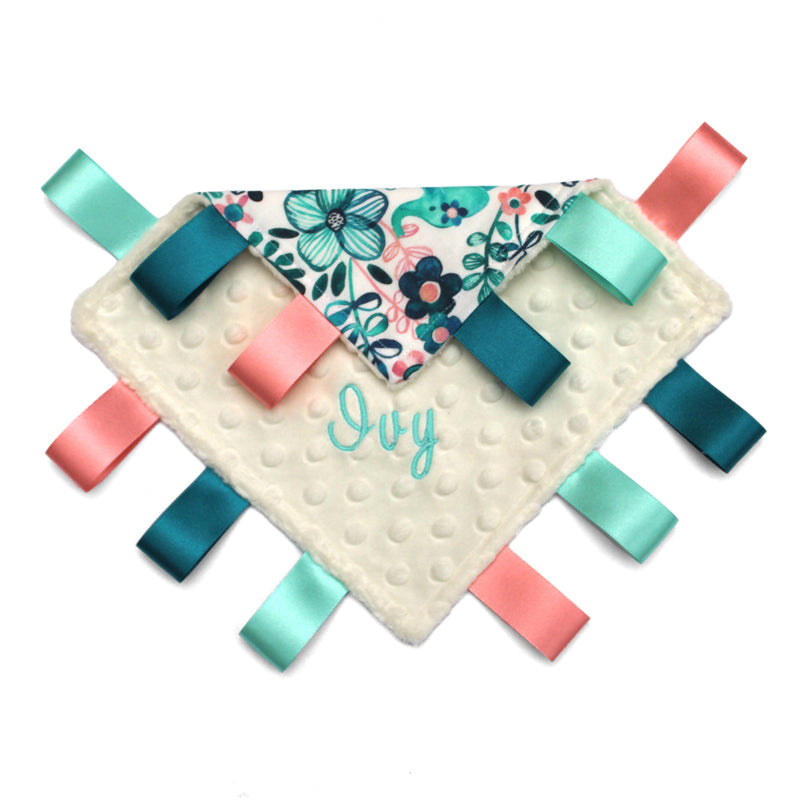 A handmade baby taggy comforter with a floral teal elephant design on a white background, backed with plush fabric and secured with ribbon tags Personalised with name Ivy