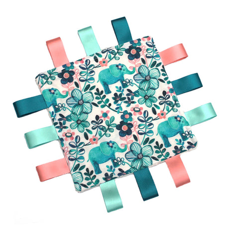 A handmade baby taggy comforter with a floral teal elephant design on a white background, backed with plush fabric and secured with ribbon tags