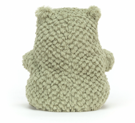 A plush toy resembling a green frog with a happy facial expression, made from a soft, textured fabric.