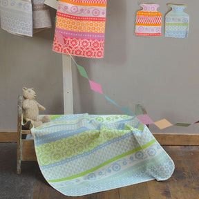 A light blue and green patterned baby blanket draped over a small wooden cot.