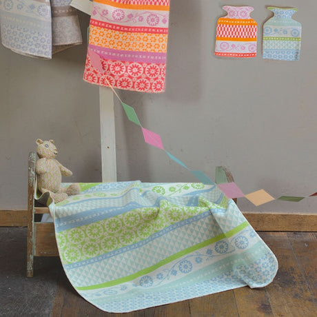 A light blue and green patterned baby blanket draped over a small wooden cot.