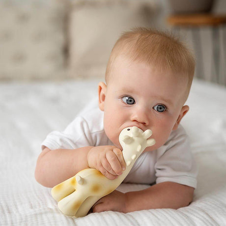 Baby biting a giraffe-shaped rubber toy on a soft surface
