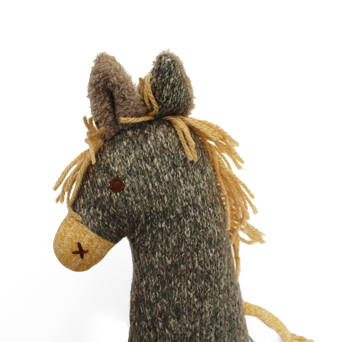 A close-up of a woolly horse knitted soft toy, showing its textured gray and beige body, yellow yarn mane, and embroidered details on a plain white background.