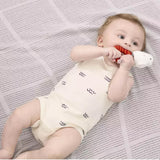 Baby lying on a textured blanket holding a A plush Harry Potter Hedwig baby ring rattle rattle with a white owl on top sitting on a red and orange striped ring.