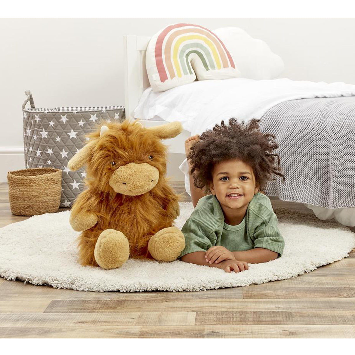 Child lying on a rug with a plush highland cow toy in a bedroom setting
