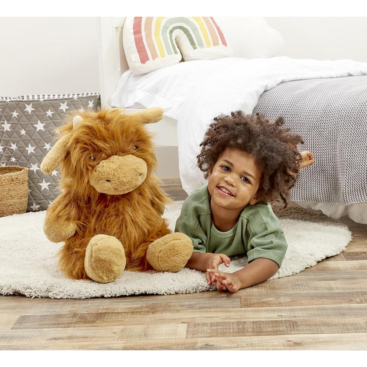 Child lying on a rug with a fluffy brown highland cow soft toy in a cozy bedroom setting